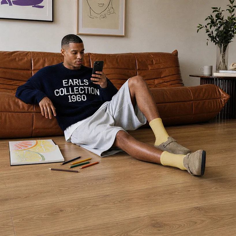 A man looking at his phone while laying on a floor laid out with 91KN732 model kiwi now floor panels