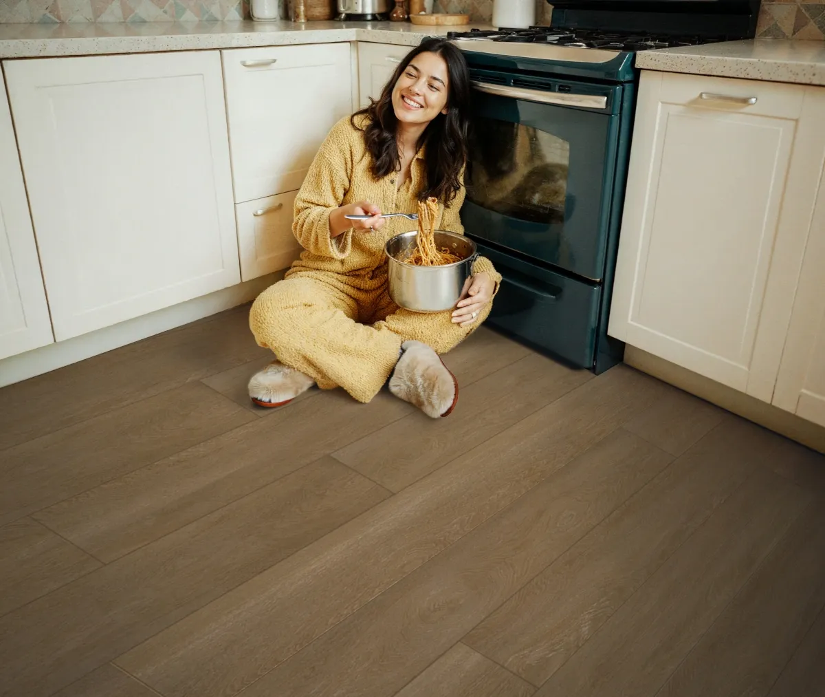 A woman eating pasta while sitting in on a kitchen floor laid out with kiwi now floor panels